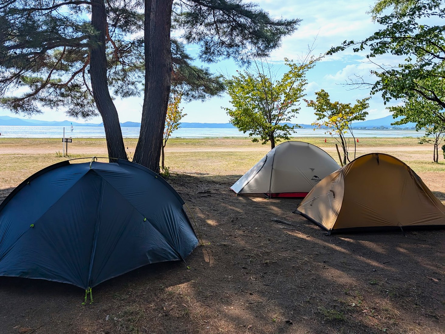 湖のキャンプ場に３つのテントが並んでいる